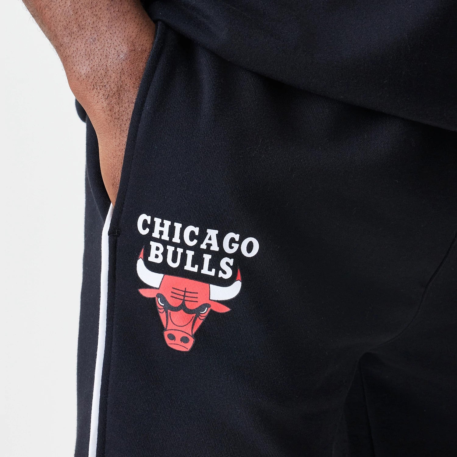 New Era Chicago Bulls NBA Piping Navy Joggers, side view with a model showing the red and white embroidered Chicago Bulls logo on the left leg, and a contrasting white stripe running down the side seam.
