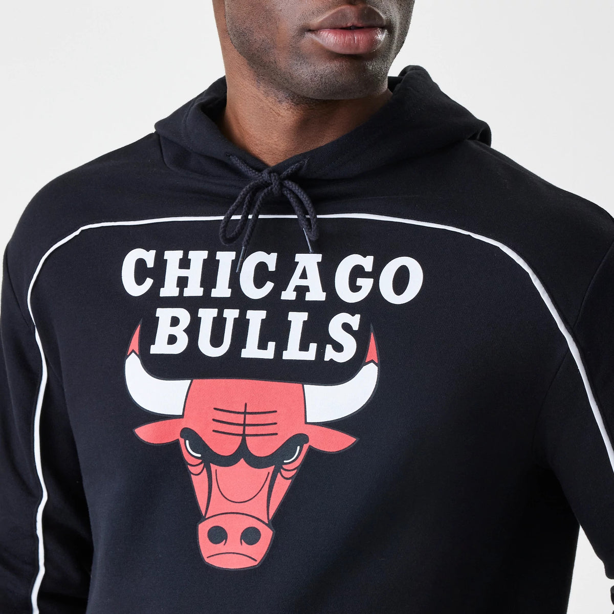 New Era Chicago Bulls NBA Piping Stripe Black Oversized Pullover Hoodie, front view on-model featuring a prominent printed Chicago Bulls logo and lettering across the chest, white piping detail along the shoulders, and a hood with drawstrings.