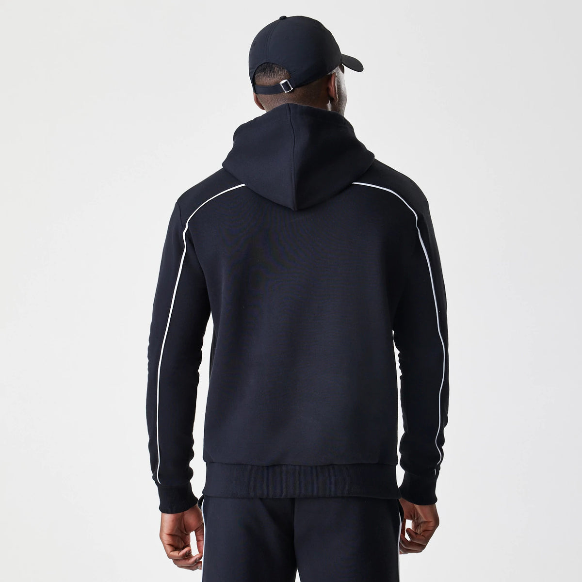 New Era Chicago Bulls NBA Piping Stripe Black Oversized Pullover Hoodie, back view on-model featuring contrasting white piping along the shoulders and sleeves, a large hood, and a relaxed fit style worn with matching black trousers and cap.