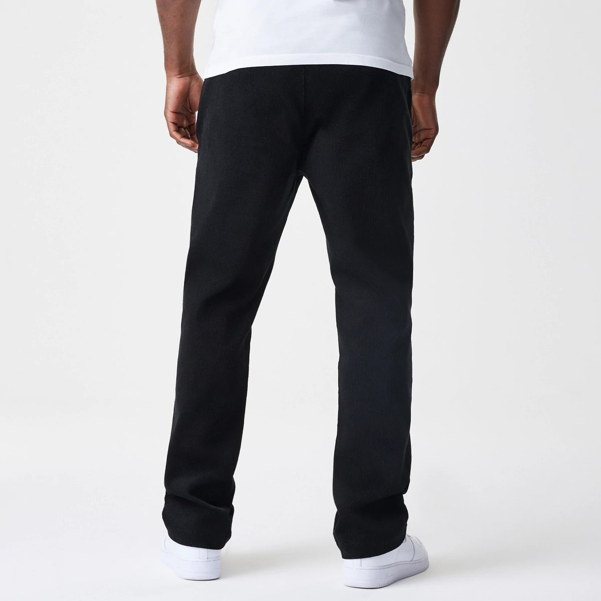 New Era Cord Black Straight Leg Chinos, rear view showing the full-length design of the black corduroy fabric, featuring a straight leg cut styled on a model with a white shirt and shoes.