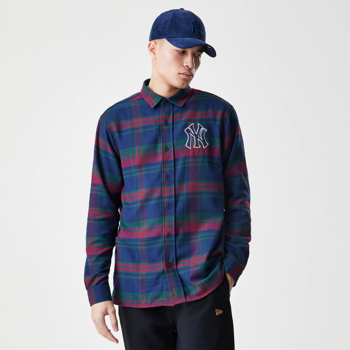 New Era New York Yankees MLB Check Navy Long Sleeve Shirt, front view on a model wearing a matching navy cap, showing a large white embroidered Yankees logo on the left chest against the navy, green and red checked pattern.