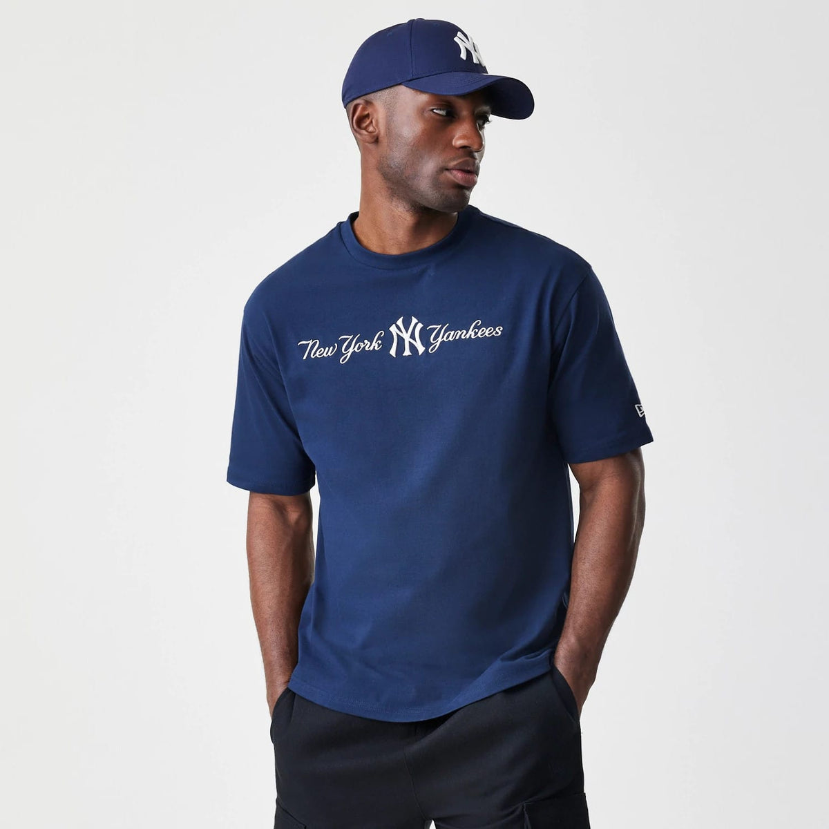New Era New York Yankees MLB Script Navy Oversized T-Shirt, front view on-model showing the white embroidered New York Yankees script across the chest, paired with a matching navy cap featuring a raised New Era logo.