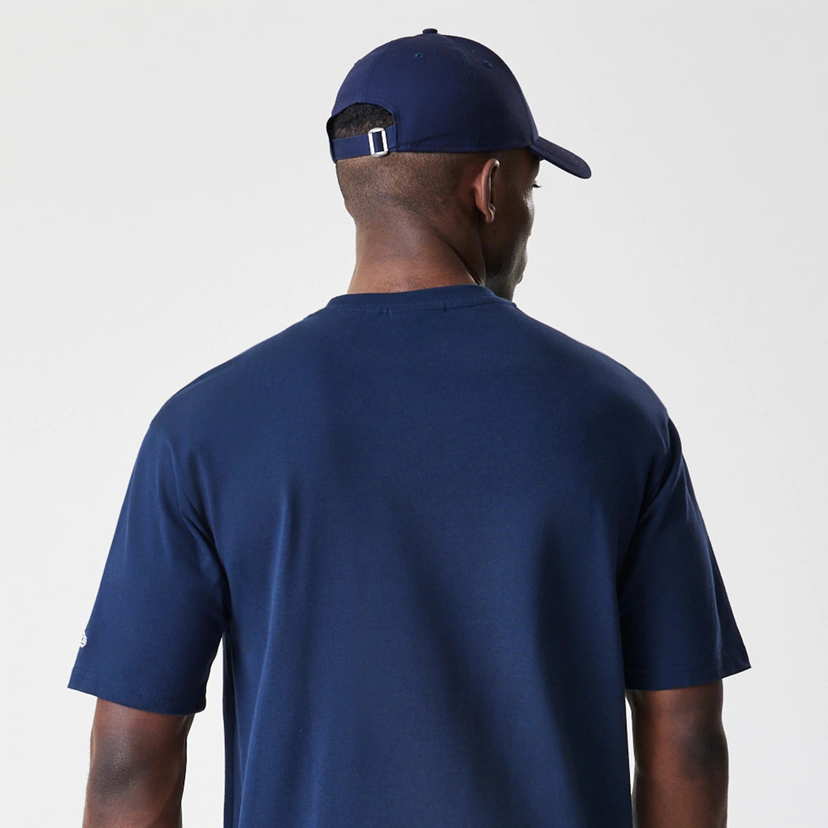 New Era New York Yankees MLB Script Navy Oversized T-Shirt, back view on a model paired with a navy cap, showing a plain navy back with short sleeves and the edge of a small embroidered New Era logo on the left sleeve.
