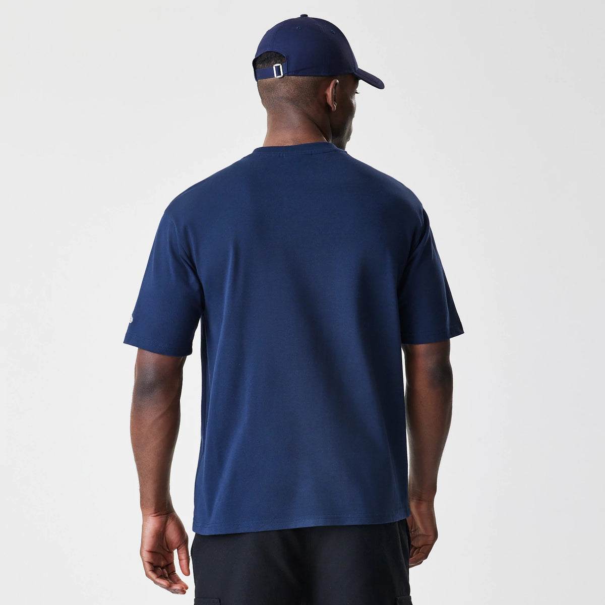 New Era New York Yankees MLB Script Navy Oversized T-Shirt, back view on a model wearing a matching navy cap, showcasing the plain navy fabric with short sleeves and an embroidered New Era logo on the left sleeve.