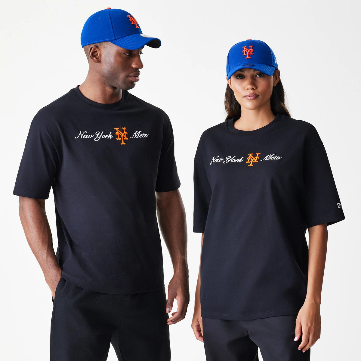 New Era New York Mets MLB Script Black Oversized T-Shirt, on-model front view showing the embroidered New York Mets script and logo in orange on the chest, both models styled with matching blue caps featuring the Mets embroidered logo.