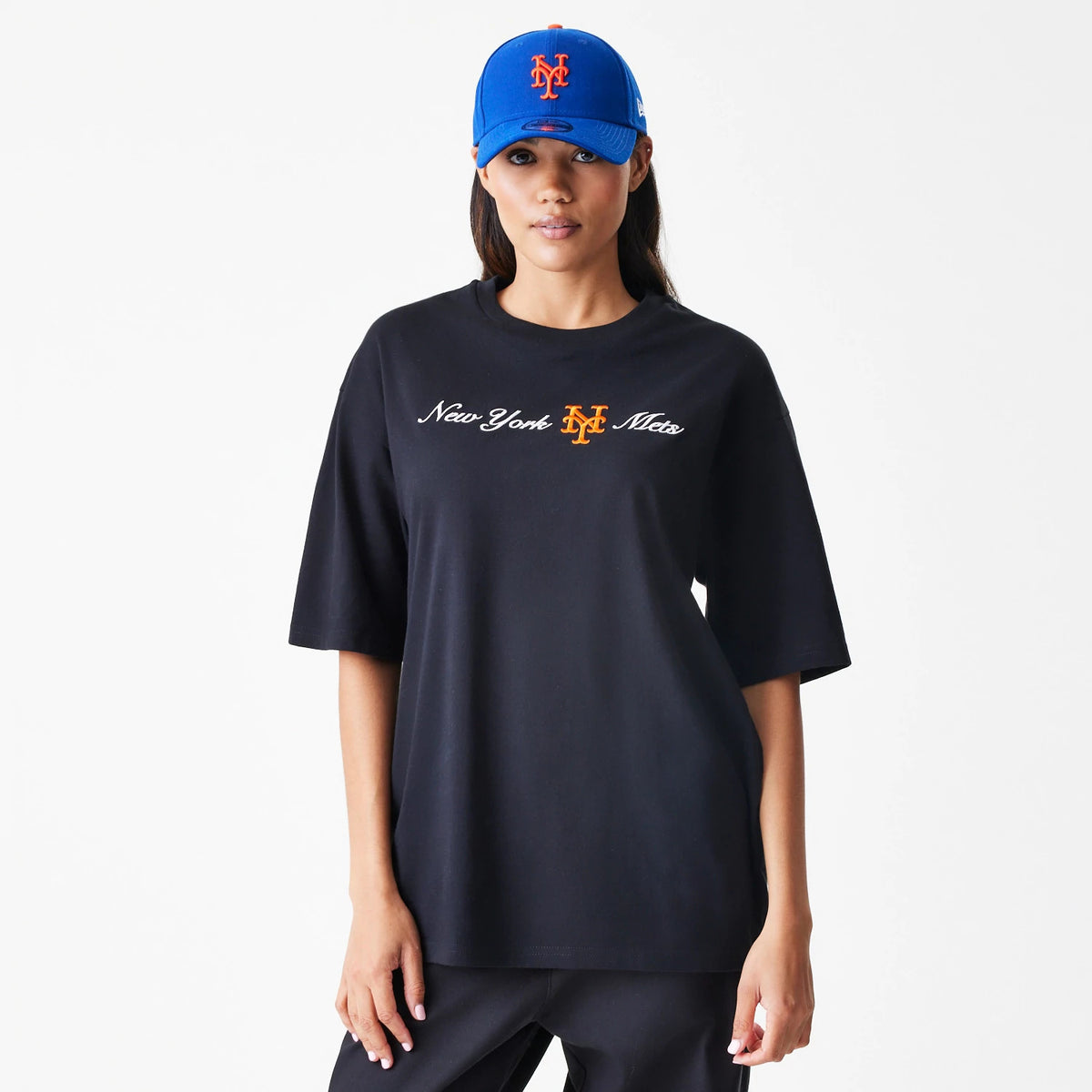 New Era New York Mets MLB Script Black Oversized T-Shirt, front view on-model displaying the embroidered New York Mets logo in orange centred between cursive white lettering across the chest, styled with a matching blue cap.