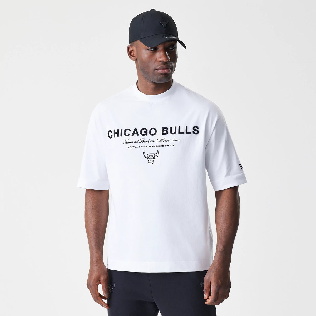 New Era Chicago Bulls NBA Linear White T-Shirt, front view on a model wearing a black cap, featuring black Chicago Bulls lettering and team logo across the chest, New Era flag embroidered on the sleeve.