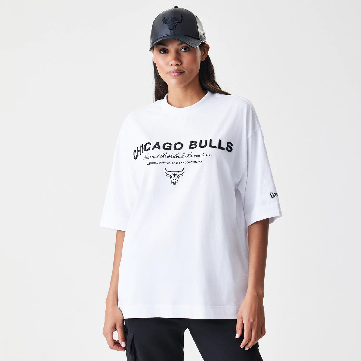 New Era Chicago Bulls NBA Linear White T-Shirt, front view on a model with a contrasting black cap, featuring black CHICAGO BULLS text across the chest, additional script below, and an embroidered New Era logo on the left sleeve.