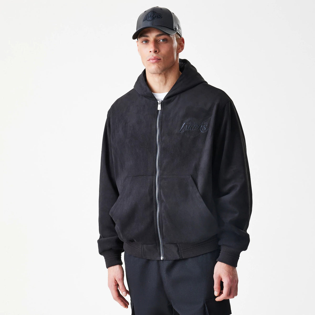 New Era LA Lakers NBA Suede Black Hooded Jacket, front view on-model showing the full zip closure and an embroidered Lakers logo on the left chest with a matching black cap on the model.