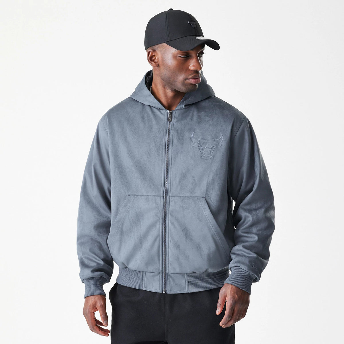 New Era Chicago Bulls NBA Suede Dark Grey Jacket, front view on-model showcasing the dark grey zip-up design with an embroidered Bulls logo on the left chest and ribbed cuffs, paired with a black cap.