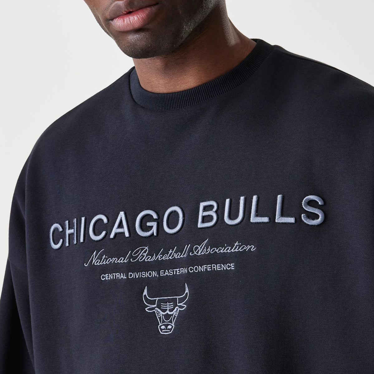 New Era Chicago Bulls NBA Linear Black Crew Neck Sweater, front view on a model showing finely embroidered Chicago Bulls lettering in grey with the team logo and additional text the team association below.