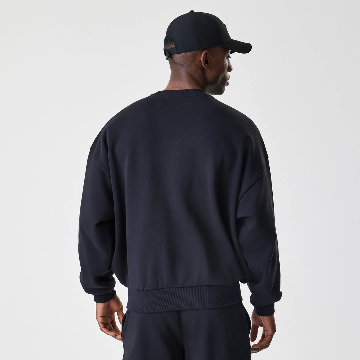 New Era Chicago Bulls NBA Linear Black Crew Neck Sweater, back view on a model displaying a loose fit with ribbed cuffs and hem, featuring a plain black back with the crew neck slightly visible.