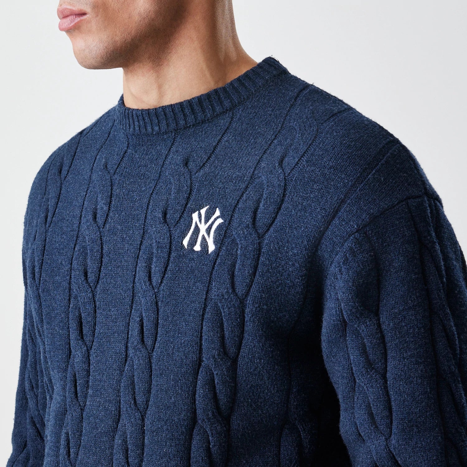 New Era New York Yankees MLB Cable Knit Navy Knitted Sweater, side view on a model showing the textured cable knit pattern with an embroidered white NY logo on the chest and a ribbed crew neck.