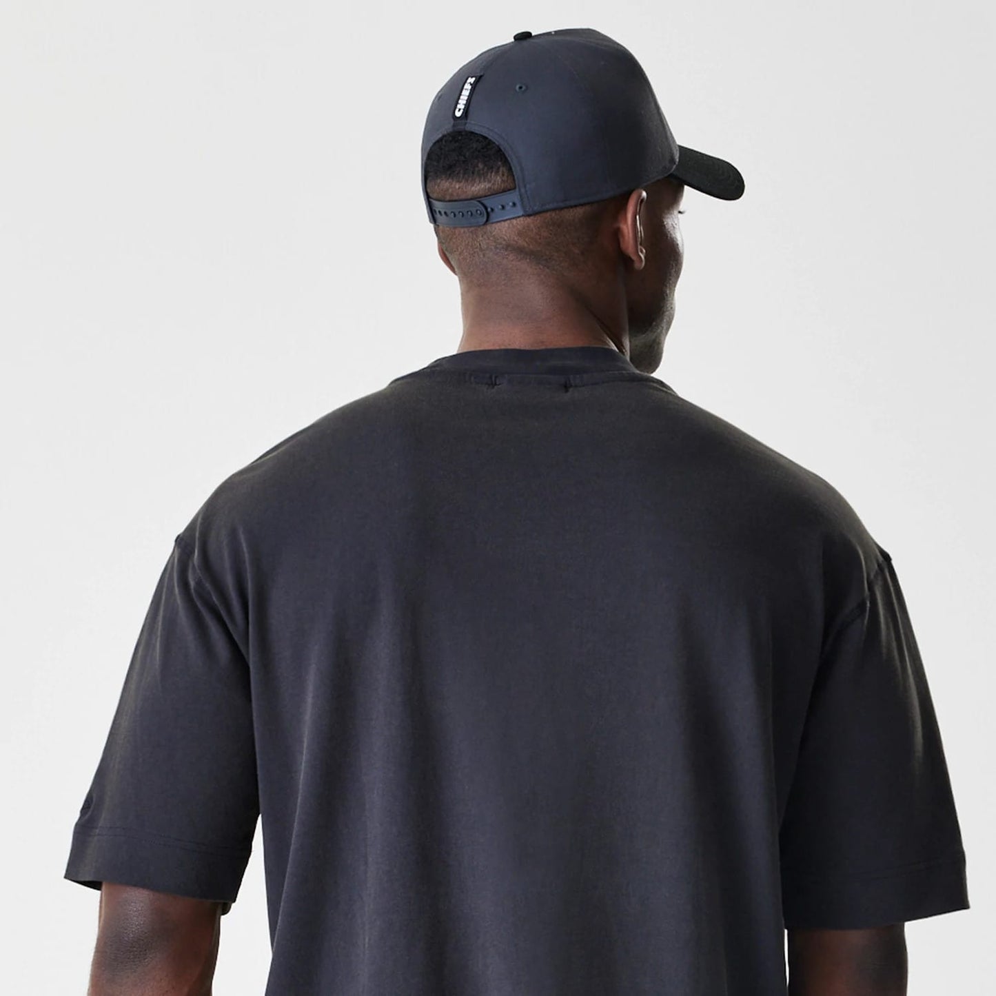 New Era Kansas City Chiefs NFL Washed Boxy Black Oversized T-Shirt, back view on a model wearing a matching cap, featuring a plain black design with relaxed boxy fit across the shoulders and sleeves.