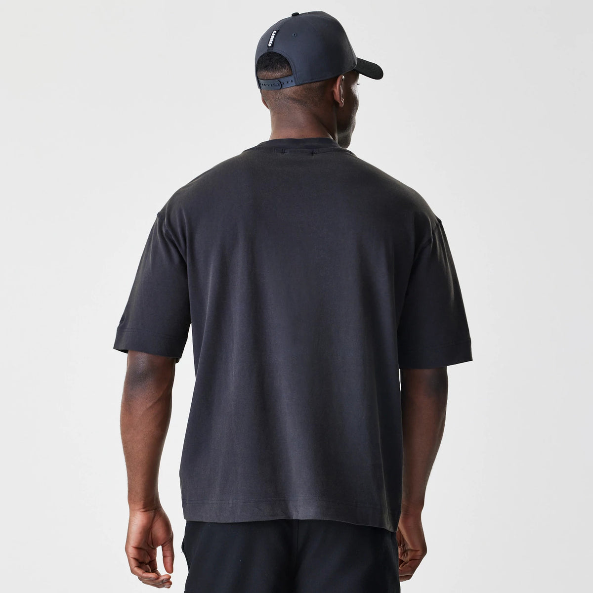 New Era Kansas City Chiefs NFL Washed Boxy Black Oversized T-Shirt, back view on-model showcasing the plain black fabric with a relaxed fit and dropped shoulder sleeves, styled with a matching black cap.