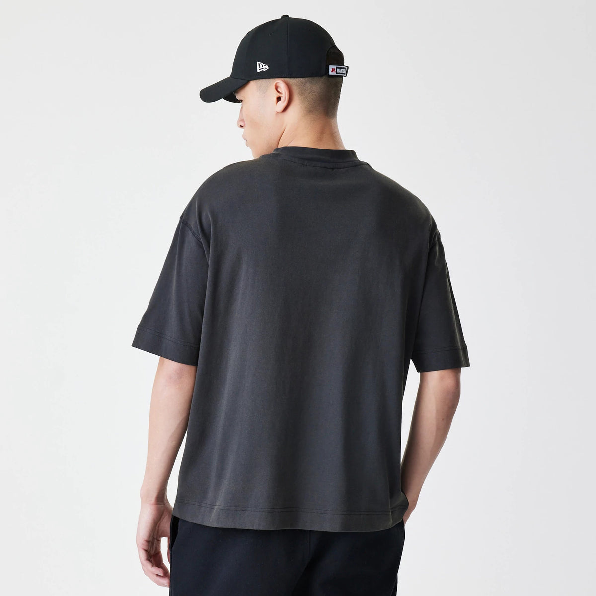 New Era Las Vegas Raiders NFL Washed Boxy Dark Grey Oversized T-Shirt, back view on a model paired with a black cap, the shirt has a plain dark grey back with short sleeves and a relaxed fit draping naturally.