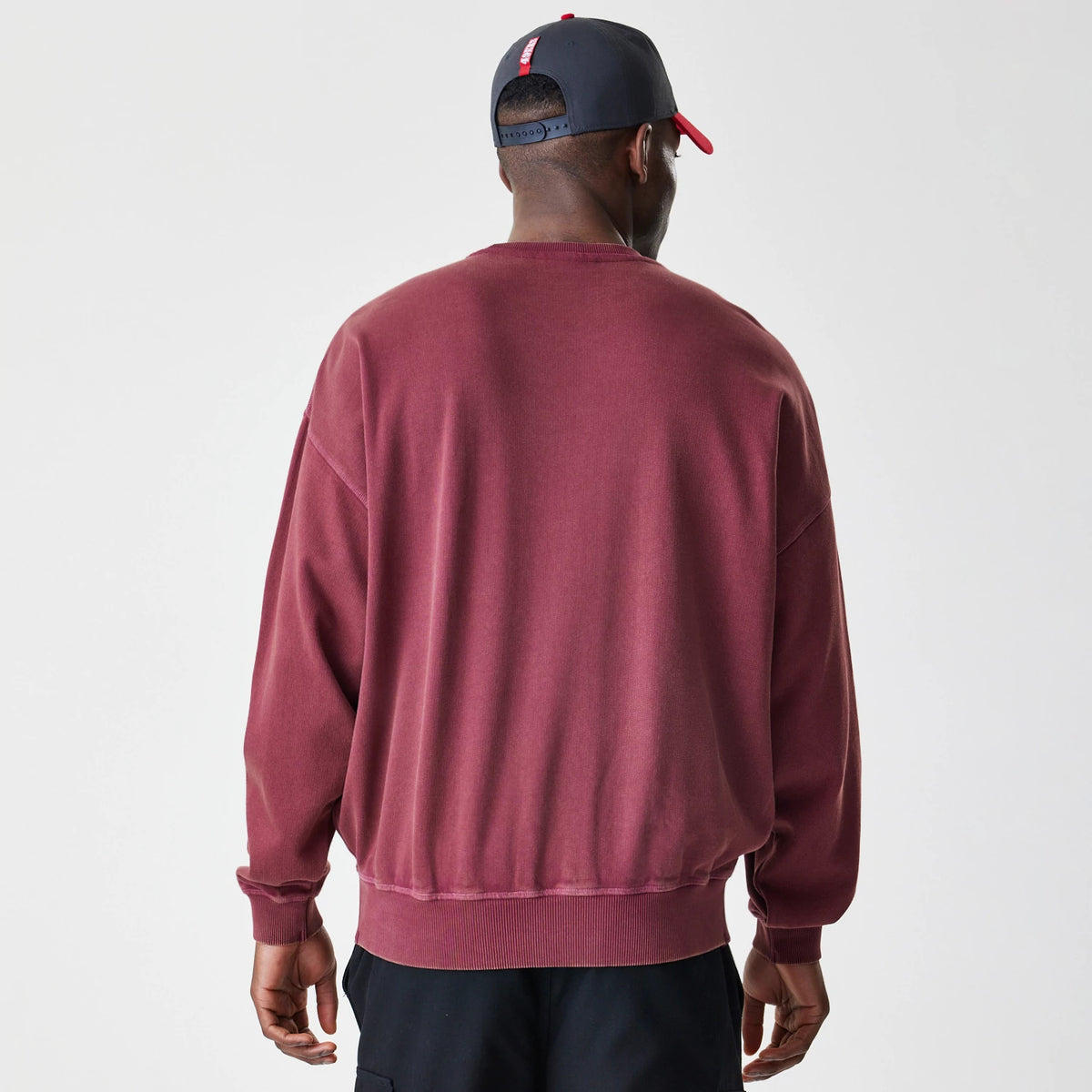New Era San Francisco 49ers NFL Washed Boxy Dark Red Oversized Crew Neck Sweater, back view on a model showing the relaxed fit and ribbed hem and cuffs, styled with a black and red cap featuring an adjustable strap.