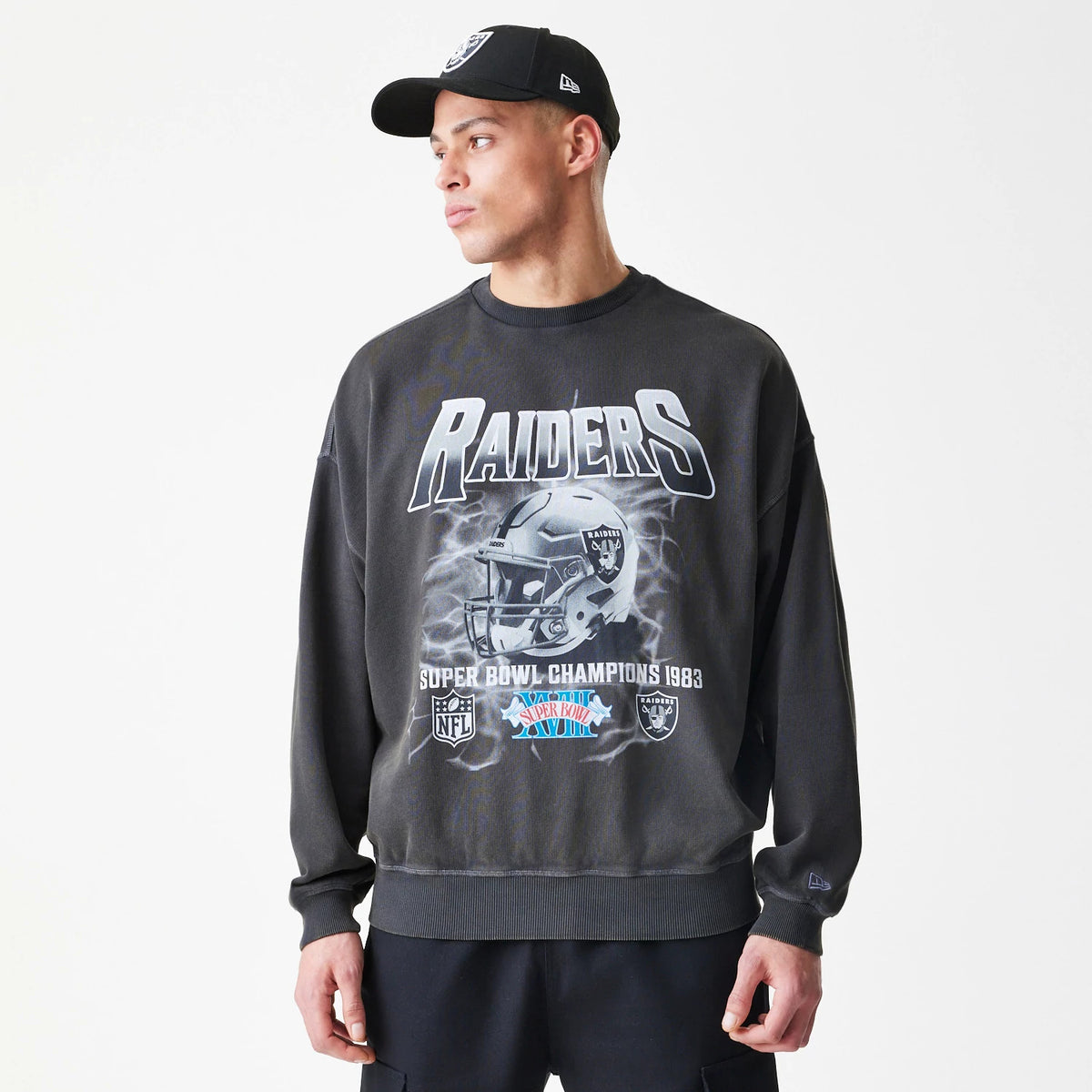 New Era Las Vegas Raiders NFL Washed Boxy Dark Grey Oversized Crew Neck Sweater, front view on a model with a matching cap, featuring a prominent Raiders graphic, helmet design and Super Bowl Champions 1983 text in contrasting white and blue.