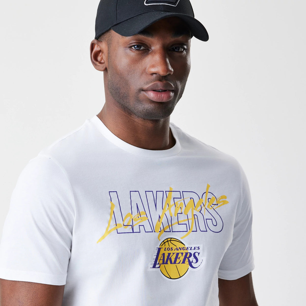New Era LA Lakers NBA Script White T-Shirt, front view on-model showing the Lakers graphic in purple with a yellow script overlay on the chest, complemented by a Los Angeles Lakers logo with a basketball motif underneath.