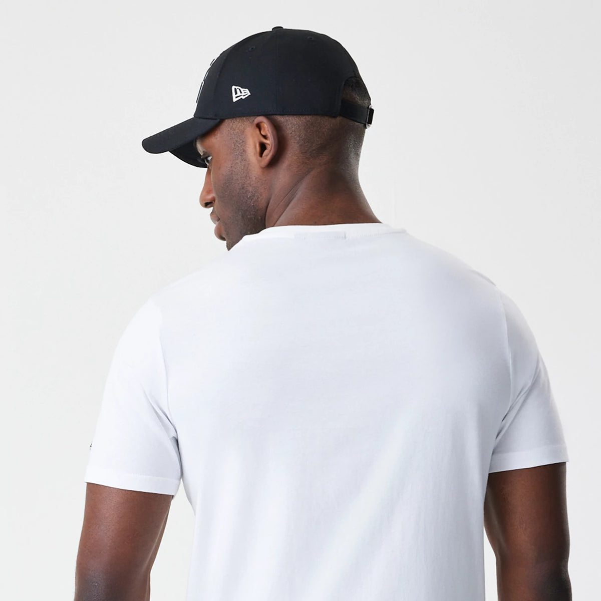 New Era LA Lakers NBA Script White T-Shirt, back view on a model with a black cap, showing the plain white fabric of the T-shirt and the cap featuring a raised New Era logo on the side.