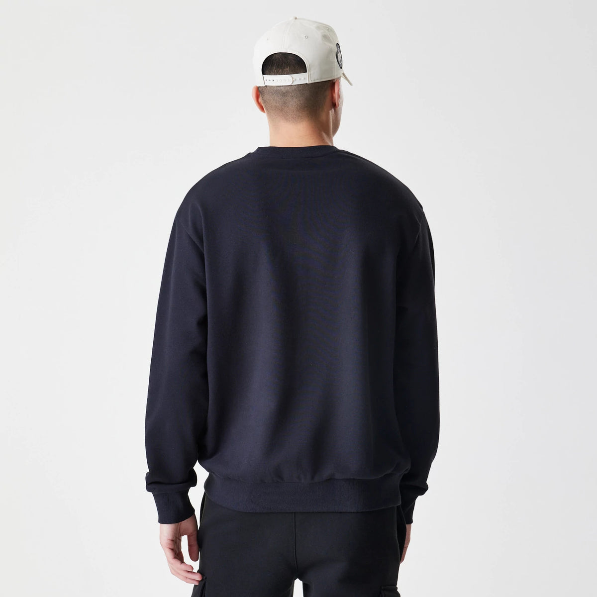 New Era New York Yankees MLB Script Black Crew Neck Sweater, back view on a model wearing a light-coloured cap, showing the plain black fabric with ribbed cuffs and hem for a casual, relaxed fit.