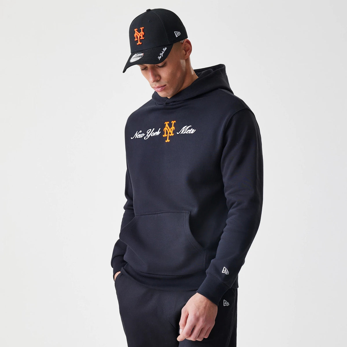New Era New York Mets MLB Script Black Oversized Pullover Hoodie, front view on-model showing embroidered orange New York Mets logo on the chest, with white script lettering, a New Era logo on the sleeve, and a kangaroo pocket at the front.