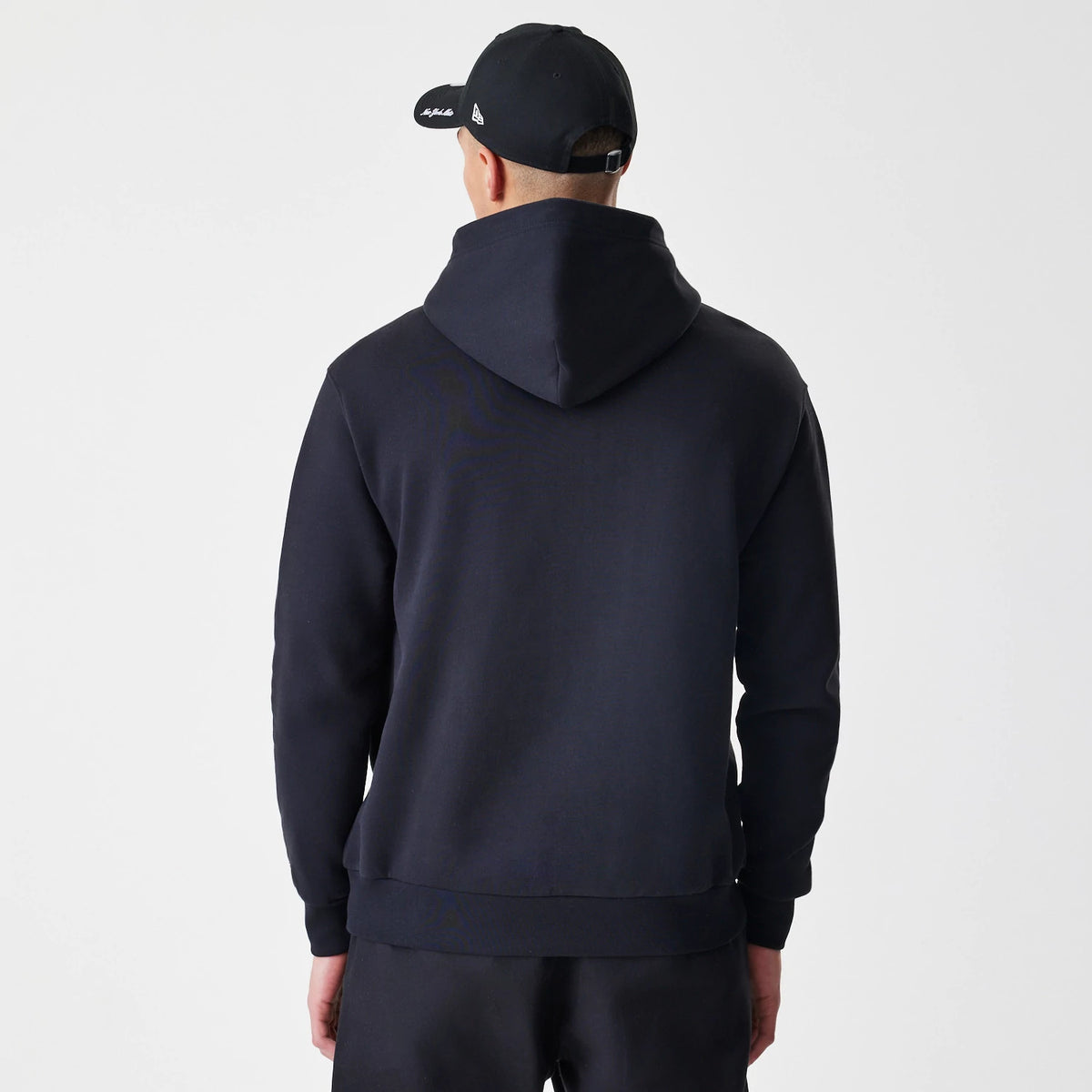 New Era New York Mets MLB Script Black Oversized Pullover Hoodie, back view on a model styled with a matching black cap, showing the oversized fit and large hood emphasising the sweatshirt's relaxed silhouette.