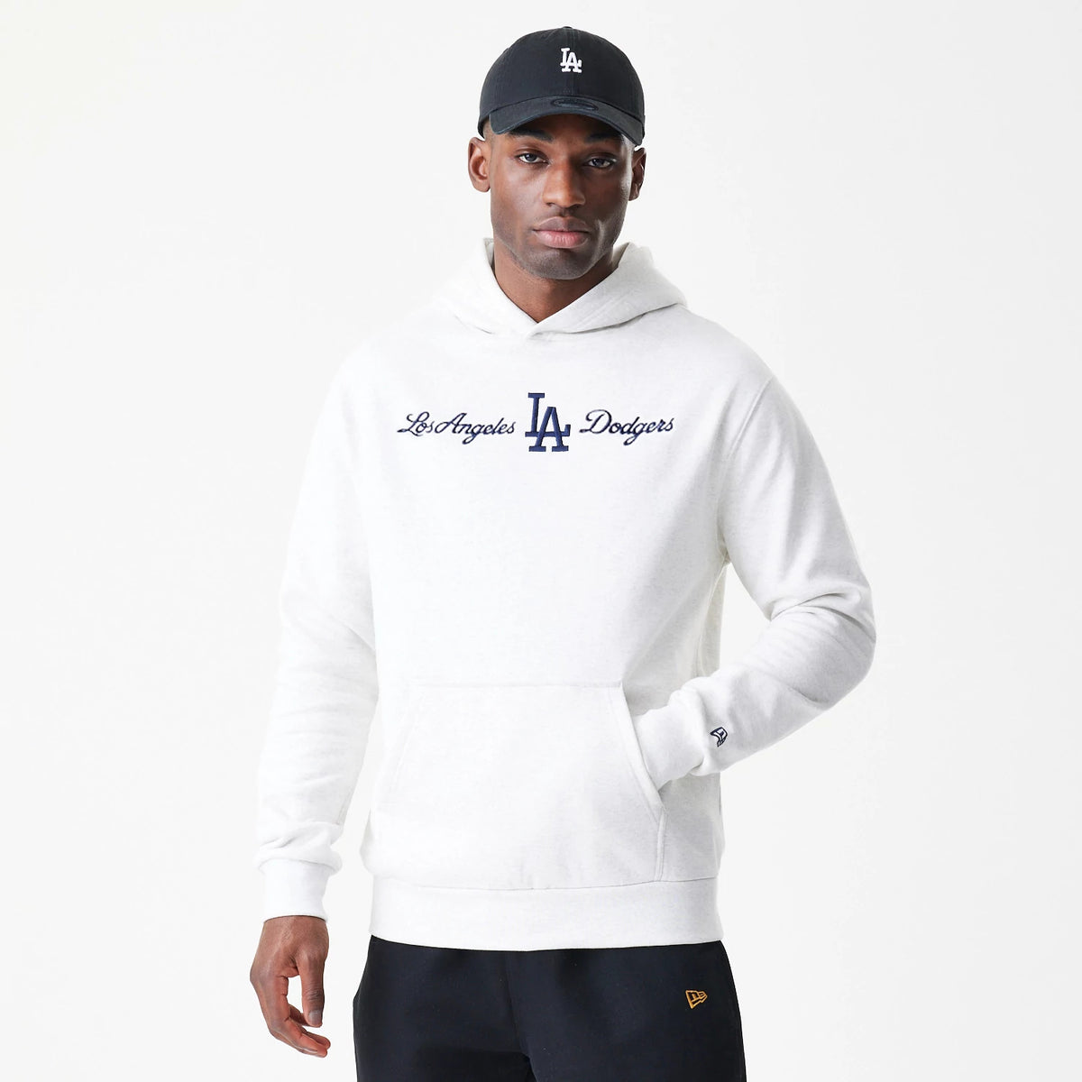 New Era LA Dodgers MLB Script White Oversized Pullover Hoodie, front view on a model with a black cap, displaying navy Los Angeles Dodgers script and the LA logo across the chest and an embroidered New Era logo on the sleeve cuff.