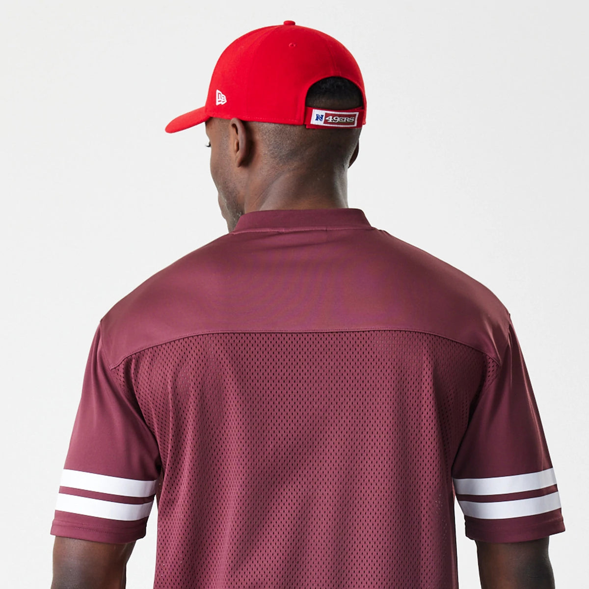 New Era San Francisco 49ers NFL Mesh Dark Red Jersey, back view on a model with a red cap, showing the dark red mesh fabric, solid yoke, and double white stripe detail on the sleeves.
