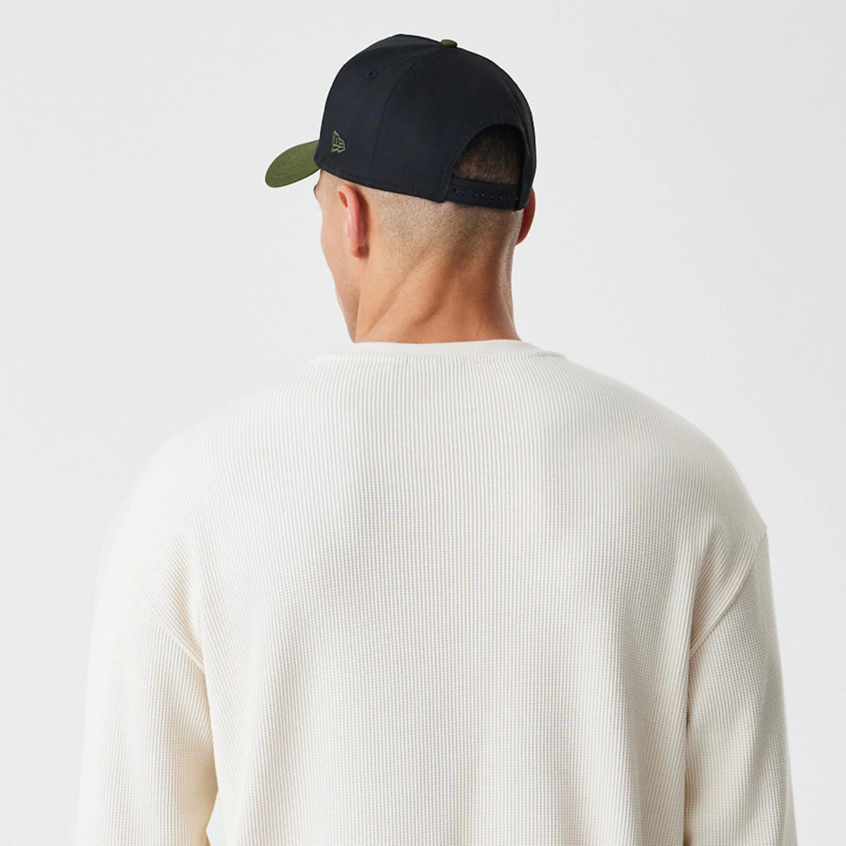 New Era Waffle Light Beige Long Sleeve T-Shirt, back view on-model showcasing the textured light beige fabric with a ribbed finish, worn with a dark cap featuring a small embossed logo on the side of the crown.