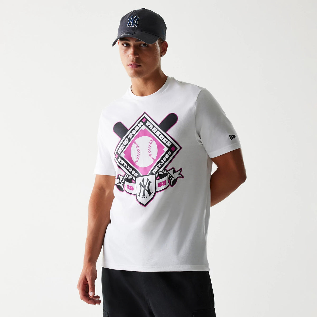 New Era New York Yankees MLB Baseball Graphic White T-Shirt, front view on a model with a dark cap, featuring a large pink and black baseball-themed graphic on the chest and a small embroidered New Era logo on the left sleeve.