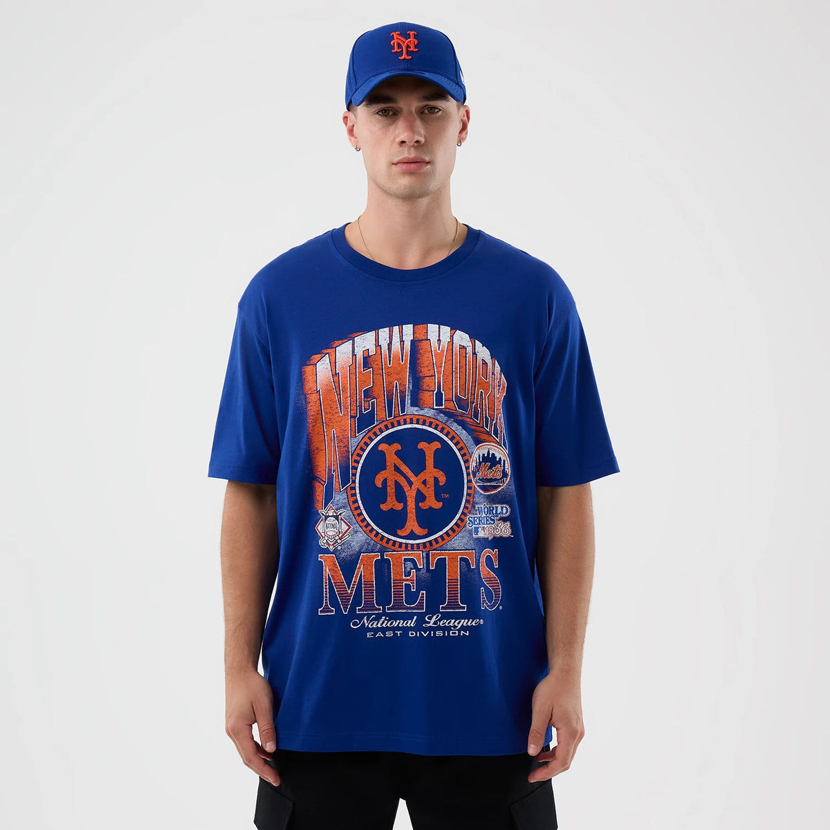 New Era New York Mets MLB Sport Classic Blue T-Shirt, front view on-model displaying a large orange New York logo graphic across the chest with Mets lettering below, styled with a matching blue cap featuring the team's logo.