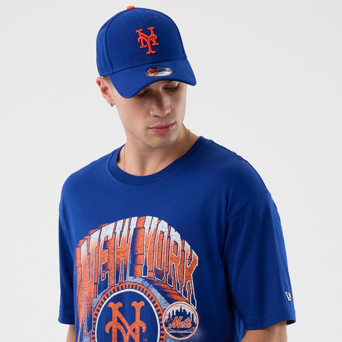 New Era New York Mets MLB Sport Classic Blue T-Shirt, front view on-model showing the New York Mets graphic in orange and white across the chest, accompanied by the raised New Era logo on the left sleeve.