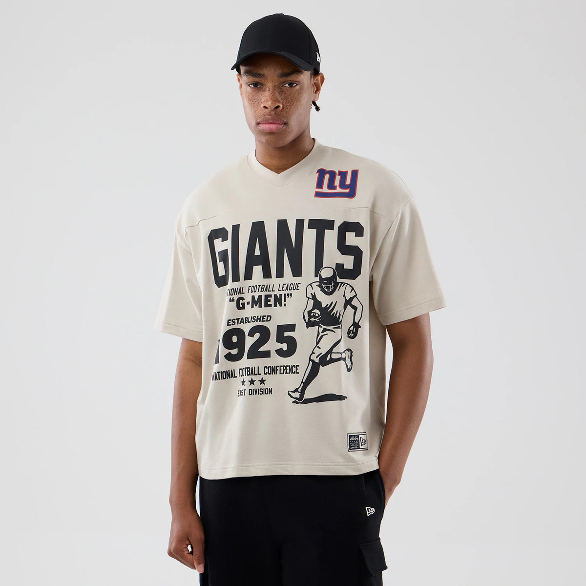New Era New York Giants NFL Throwback Prep Light Beige T-Shirt, front view showing black Giants lettering, a vintage football player graphic, and a woven New Era logo patch at the bottom left hem.