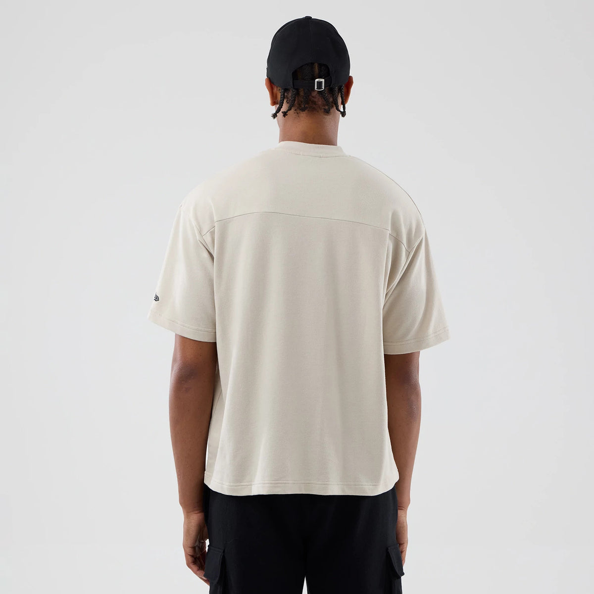 New Era New York Giants NFL Throwback Prep Light Beige T-Shirt, back view on a model wearing a black cap, showing the plain light beige back panel with relaxed short sleeves and an embroidered New Era logo on the left sleeve near the hem.