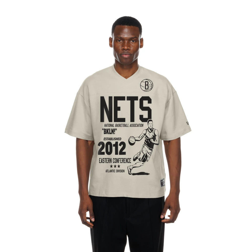 New Era Brooklyn Nets NBA Throwback Prep Light Beige T-Shirt, front view on a model showing a large black printed graphic of a basketball player and text including NETS, the number 2012, and a circular logo at the top left.