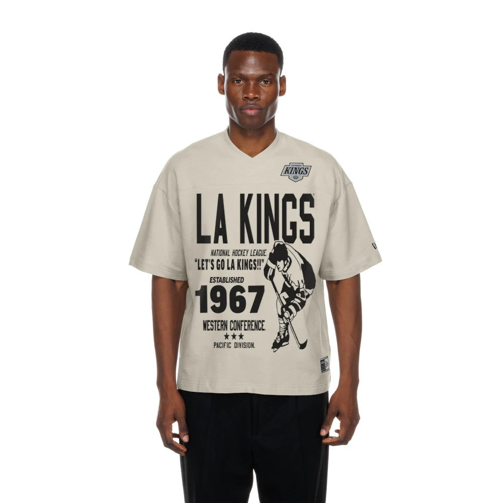 New Era LA Kings NHL Throwback Prep Light Beige T-Shirt, front view on a model showing large black LA Kings text and sports graphics on the chest, a small team logo embroidered on the upper left, and a straight hemline.