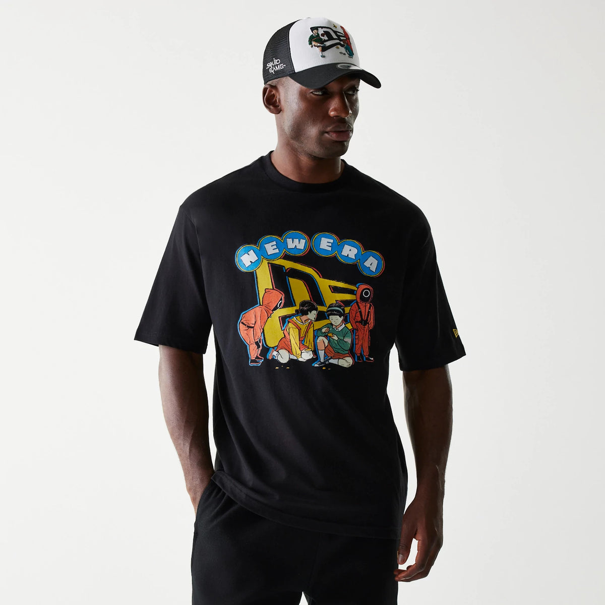 New Era Netflix Squid Game Black Oversized T-Shirt, front view on a model with matching black cap, featuring a graphic of Squid Game characters on the chest, highlighted by a blue and yellow New Era design above.