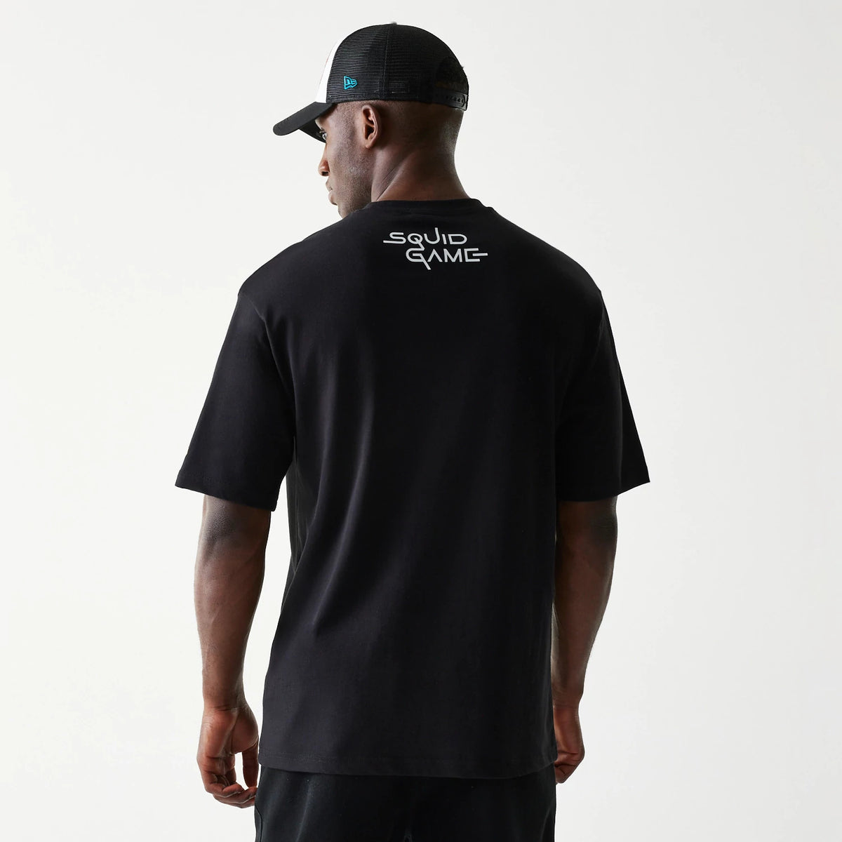 New Era Netflix Squid Game Black Oversized T-Shirt, back view on a model showing the white Squid Game lettering centred near the top on a plain black fabric, with short sleeves and a relaxed fit.