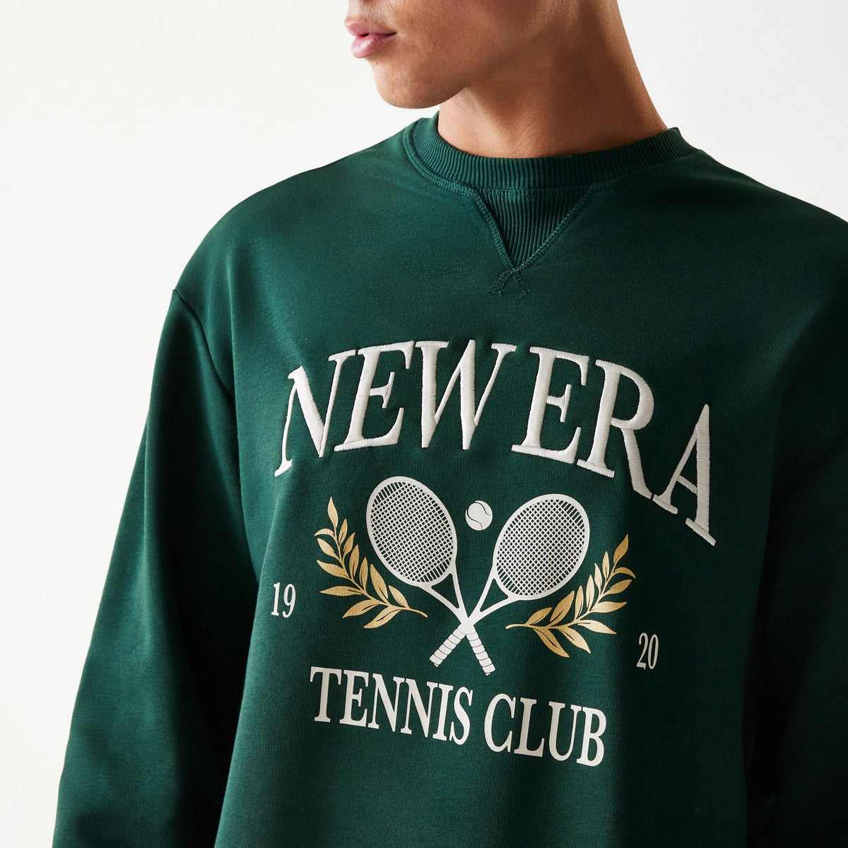 New Era Dark Green Oversized Crew Neck Sweater, front view with white embroidered 'New Era Tennis Club' lettering, tennis racket graphic, and gold laurel details on the chest of the dark green fabric.