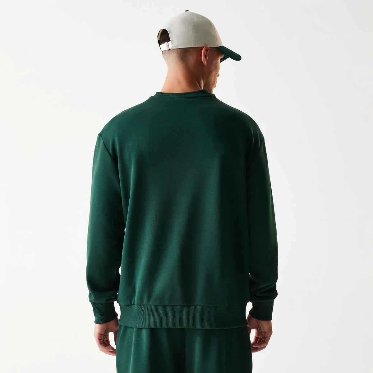 New Era Dark Green Oversized Crew Neck Sweater, rear view on a model showing the relaxed fit with ribbed hem and cuffs, offering a glimpse of matching green trousers for a coordinated look.