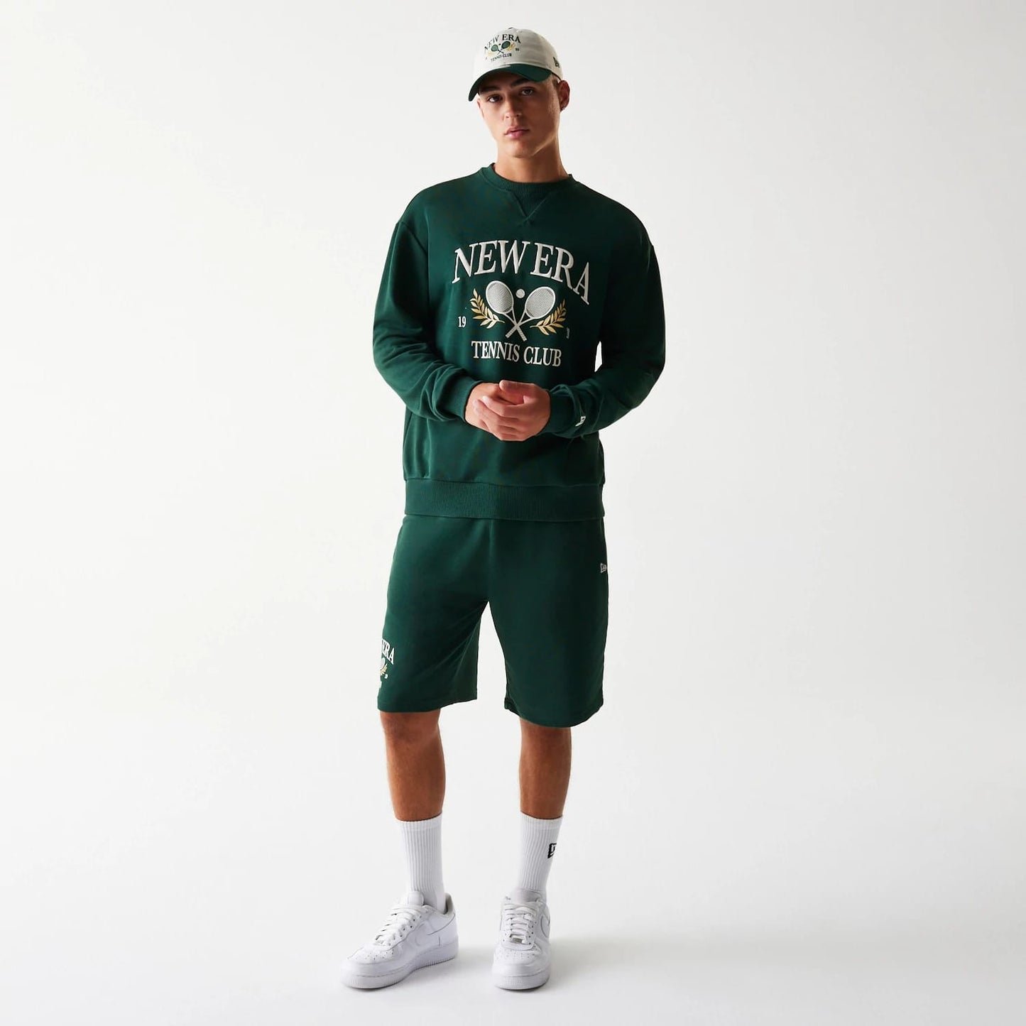 New Era Dark Green Oversized Crew Neck Sweater, front view on a model with matching dark green shorts, featuring large white and gold embroidered New Era Tennis Club graphics across the chest.