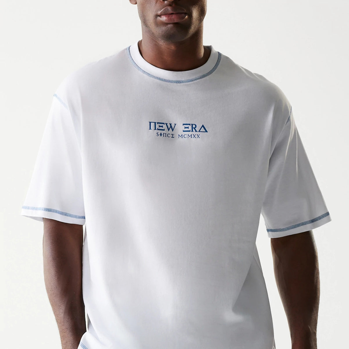 New Era Orthodox Church White Oversized T-Shirt, front view on-model featuring a white base with blue embroidered New Era logo centred on the chest, short sleeves, and blue stitching detail along the neckline and cuffs.