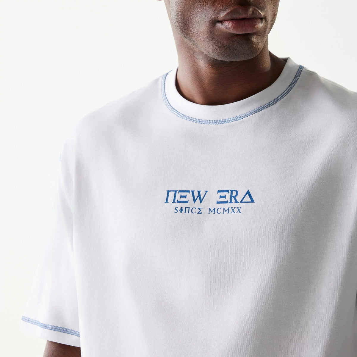 New Era Orthodox Church White Oversized T-Shirt, front view on-model showing a blue embroidered New Era logo and since lettering on the centre chest, with blue stitching around the crew neck and sleeve hems.