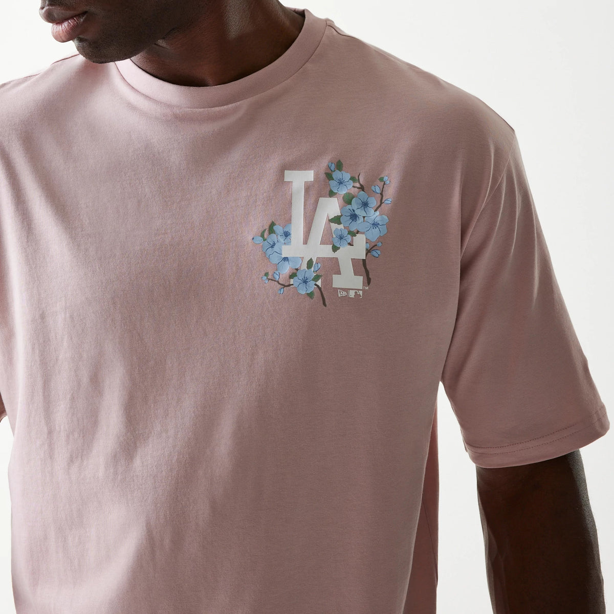 New Era LA Dodgers MLB Floral Pastel Pink Oversized T-Shirt, front view on-model featuring a white embroidered LA logo with surrounding blue floral graphics on the left chest, set against a pastel pink background.