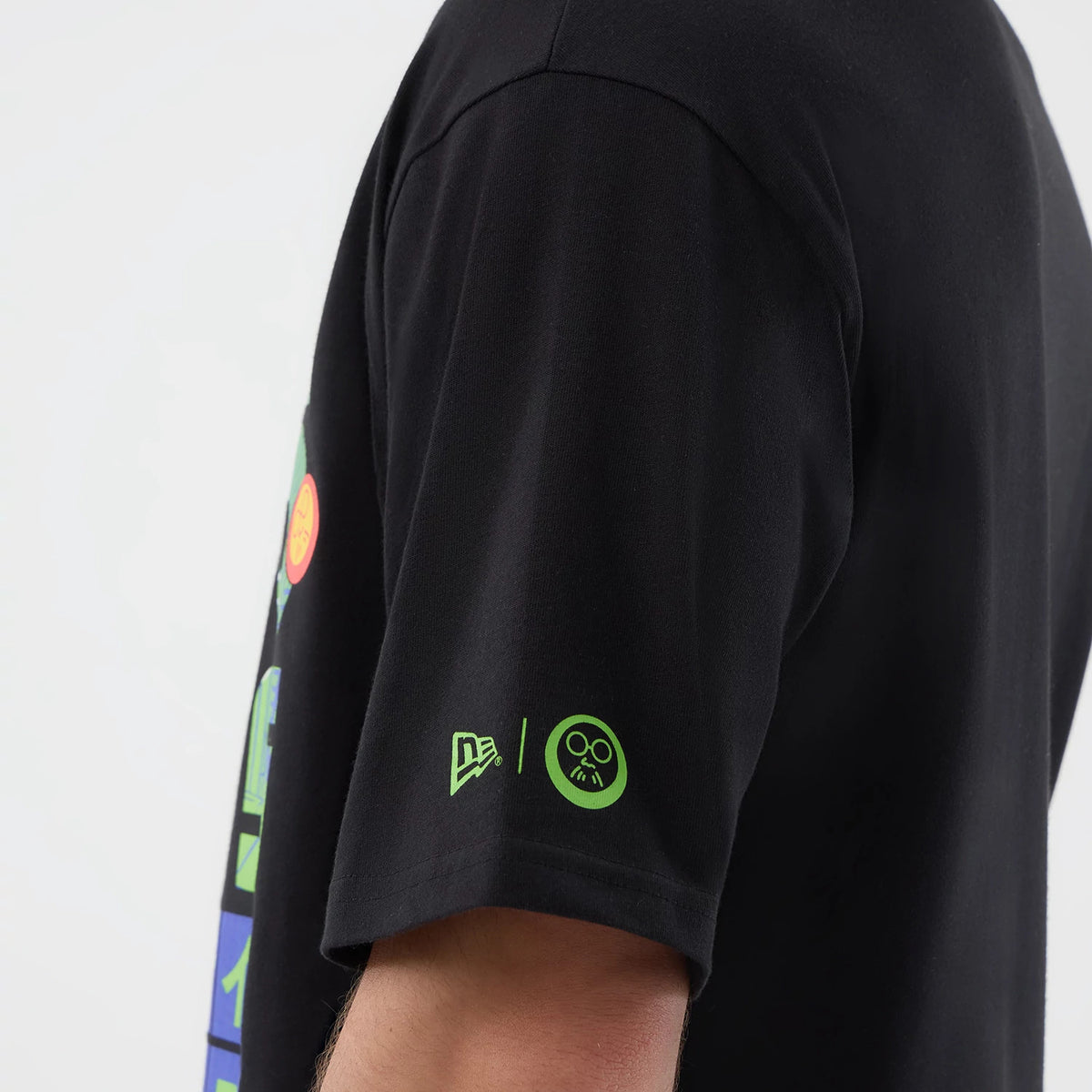 New Era Sakamoto Days Netflix Black T-Shirt, three-quarter view focusing on the right sleeve worn by a model, featuring a green printed New Era logo near the cuff and colourful graphics extending along the side of the garment.