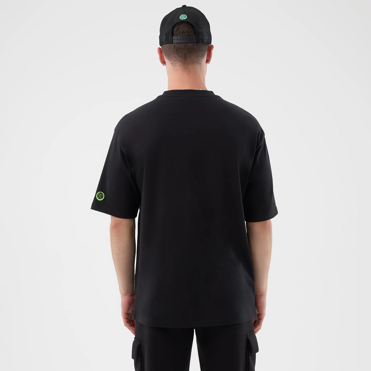New Era Sakamoto Days Netflix Black T-Shirt, back view on-model showing a black tee with a small green embroidered logo on the left sleeve and a matching black cap with a circular green embroidered logo at the centre back.
