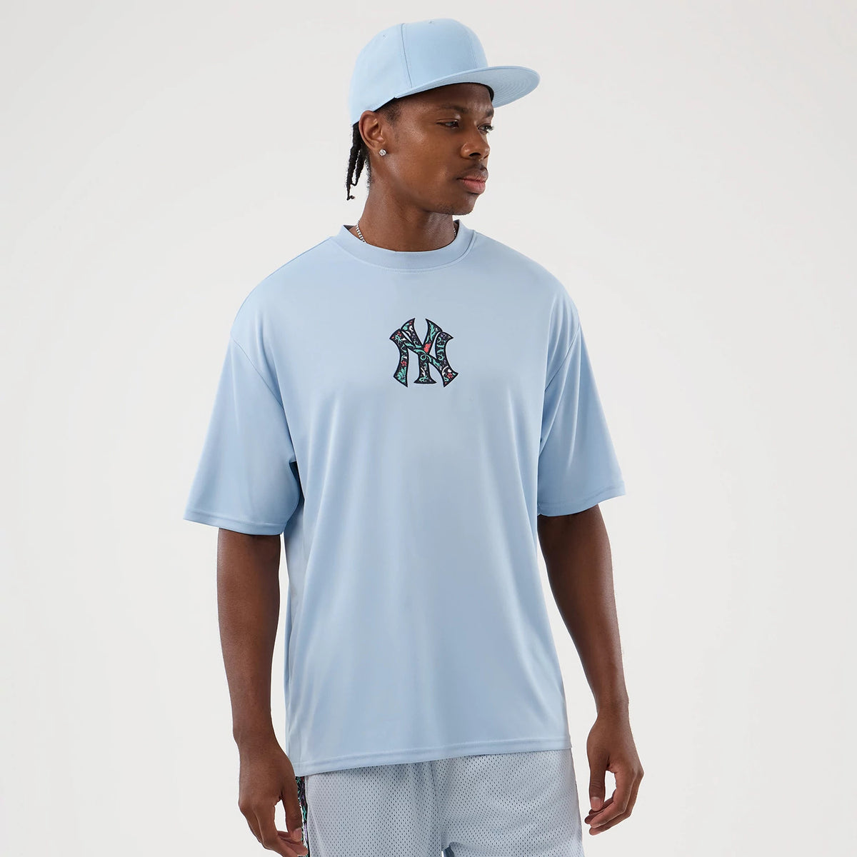 New Era New York Yankees MLB Mesh Infill Pastel Blue Oversized T-Shirt, front view on a model wearing a matching cap, featuring a central embroidered Yankees logo with a colourful mesh infill pattern on the chest against the pastel blue fabric.