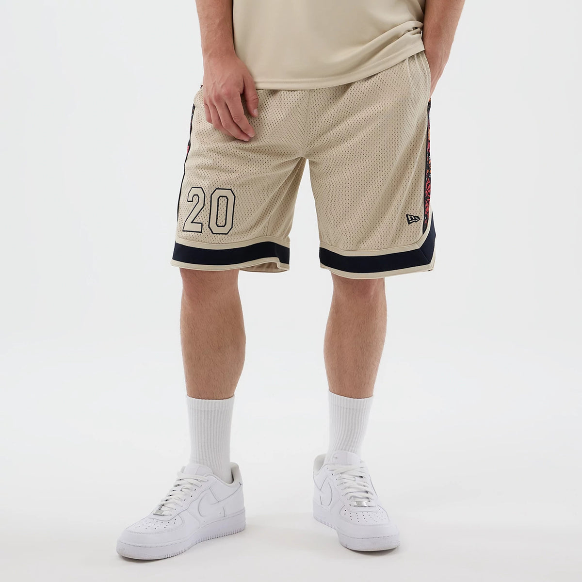 New Era Mesh Light Beige Mesh Shorts, front view on-model showing the embroidered number 20 on the left leg, black trim at the hem and the New Era logo on the lower right leg, styled with white athletic shoes and socks.
