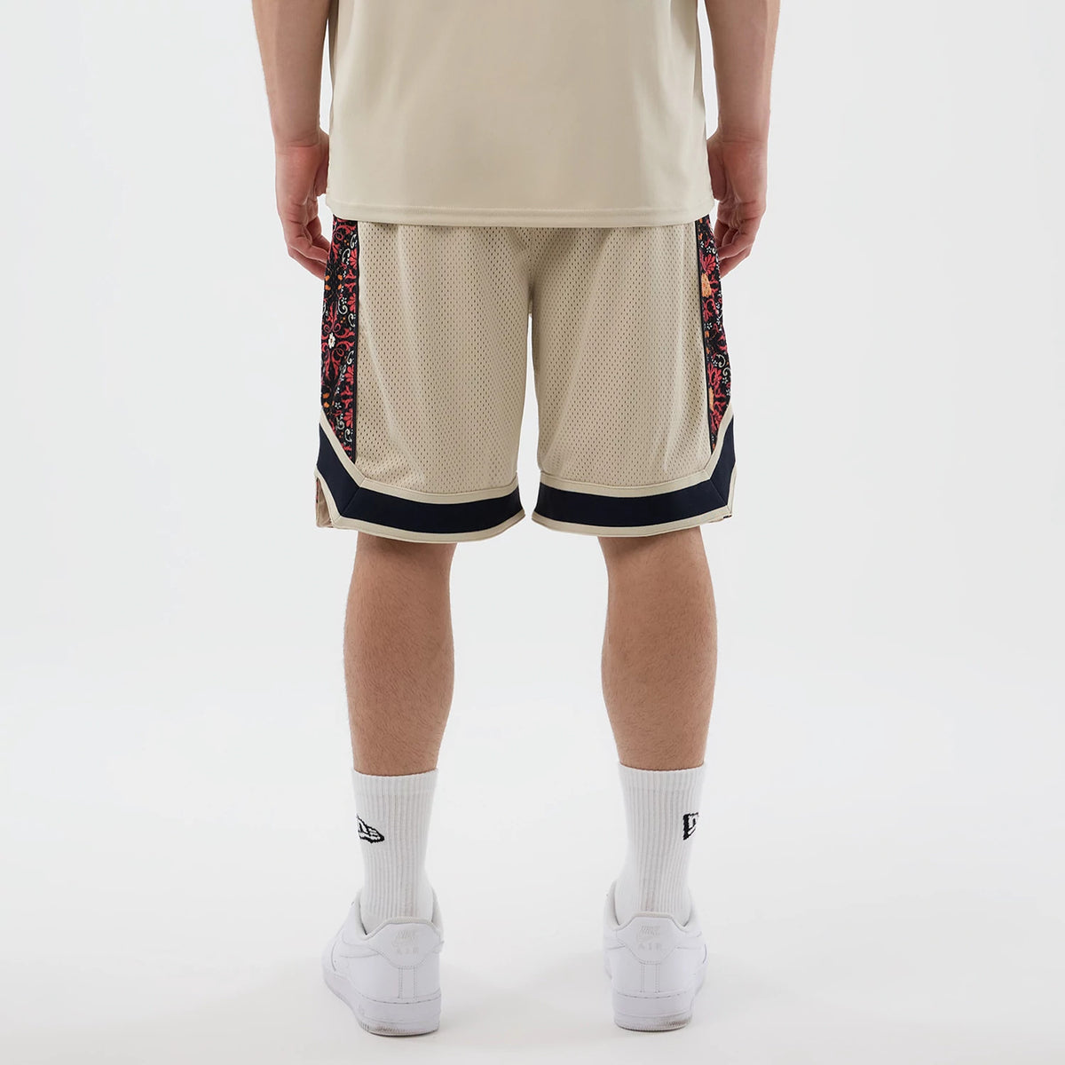 New Era Mesh Light Beige Mesh Shorts, back view on a model showcasing beige mesh fabric with intricate patterned side panels and black trim at the hems, complemented by white socks with an embroidered New Era logo.